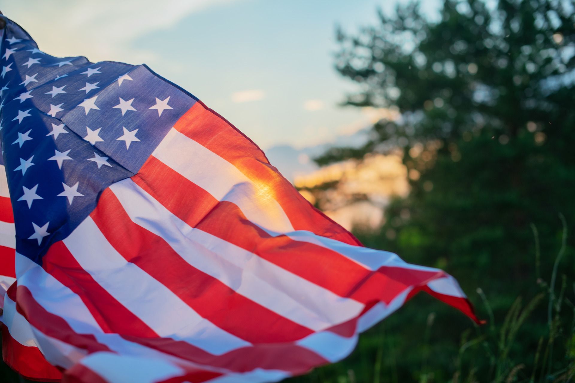 A man in a military uniform is holding an american flag in his hands.