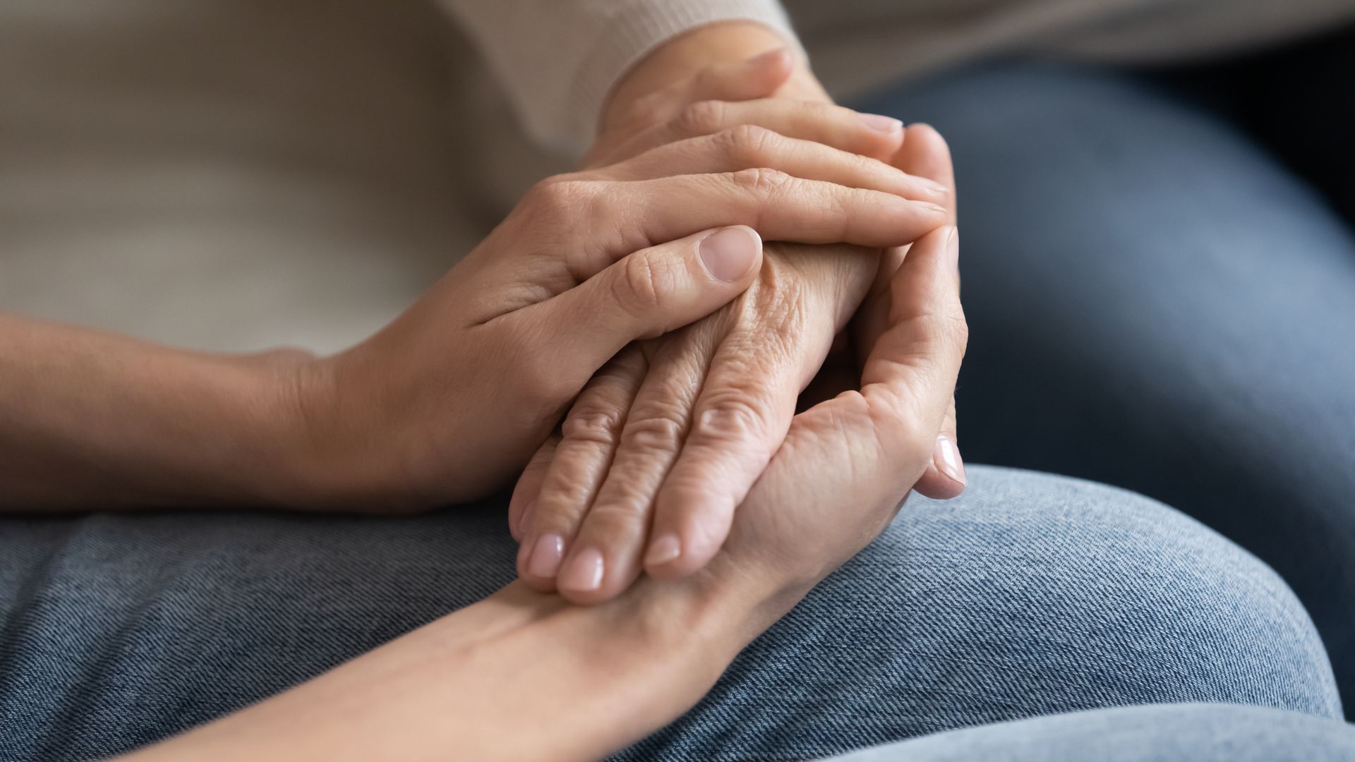 Two hands, one older, resting in a younger person's hands, showing support and care.