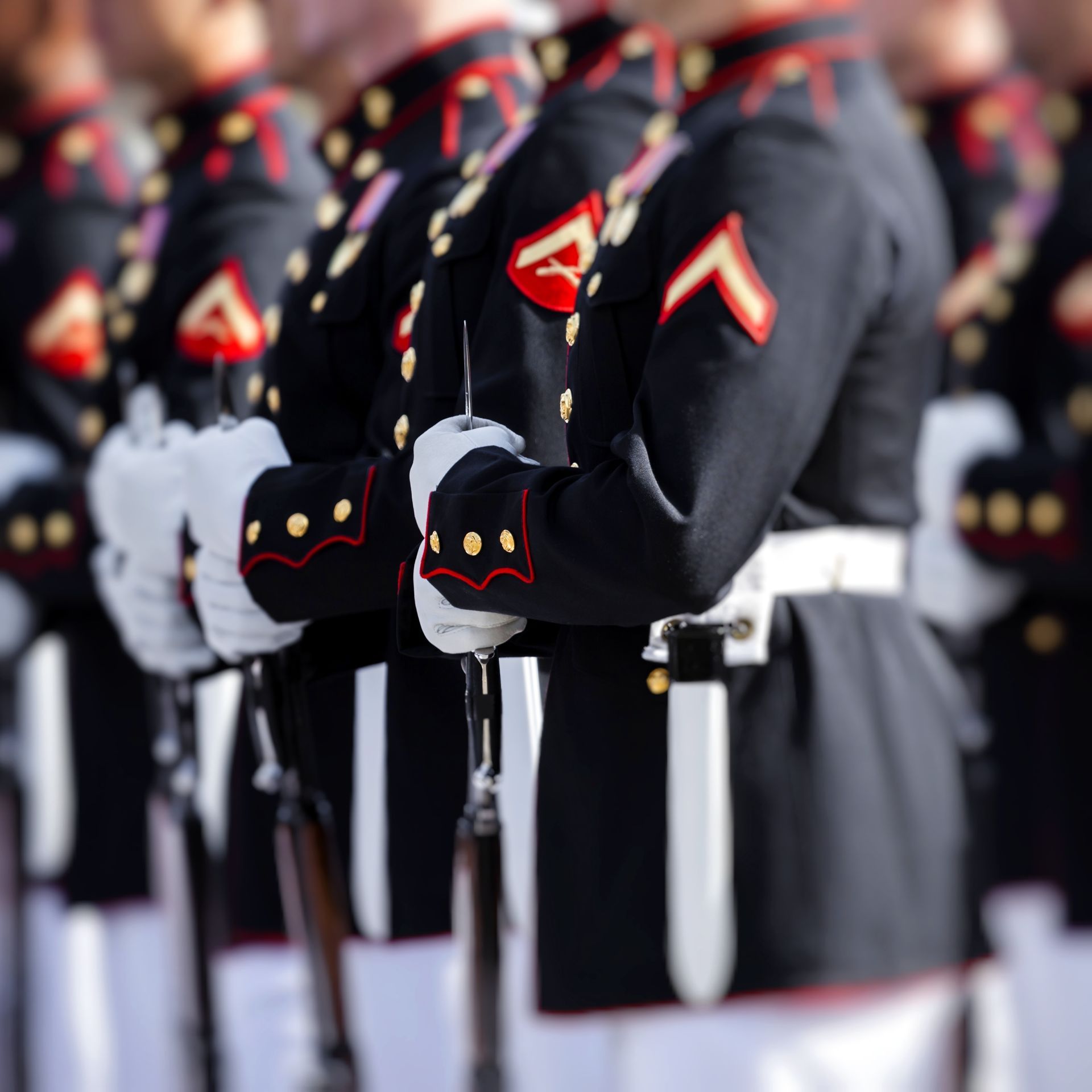 Marines in dress blues stand at attention. Dark blue uniforms, white gloves, red and gold accents.