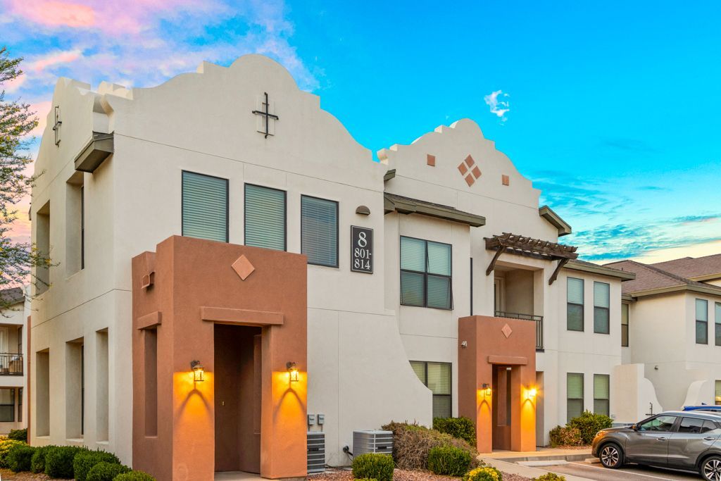 A white building with a cross on the top of it and cars parked in front of it.