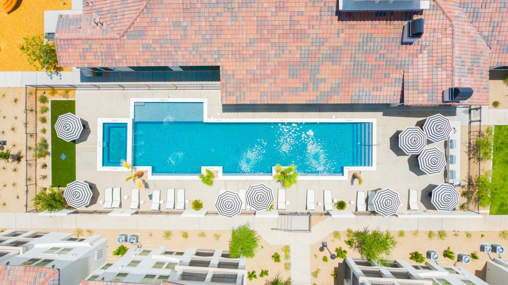 An aerial view of a large swimming pool surrounded by umbrellas and palm trees.