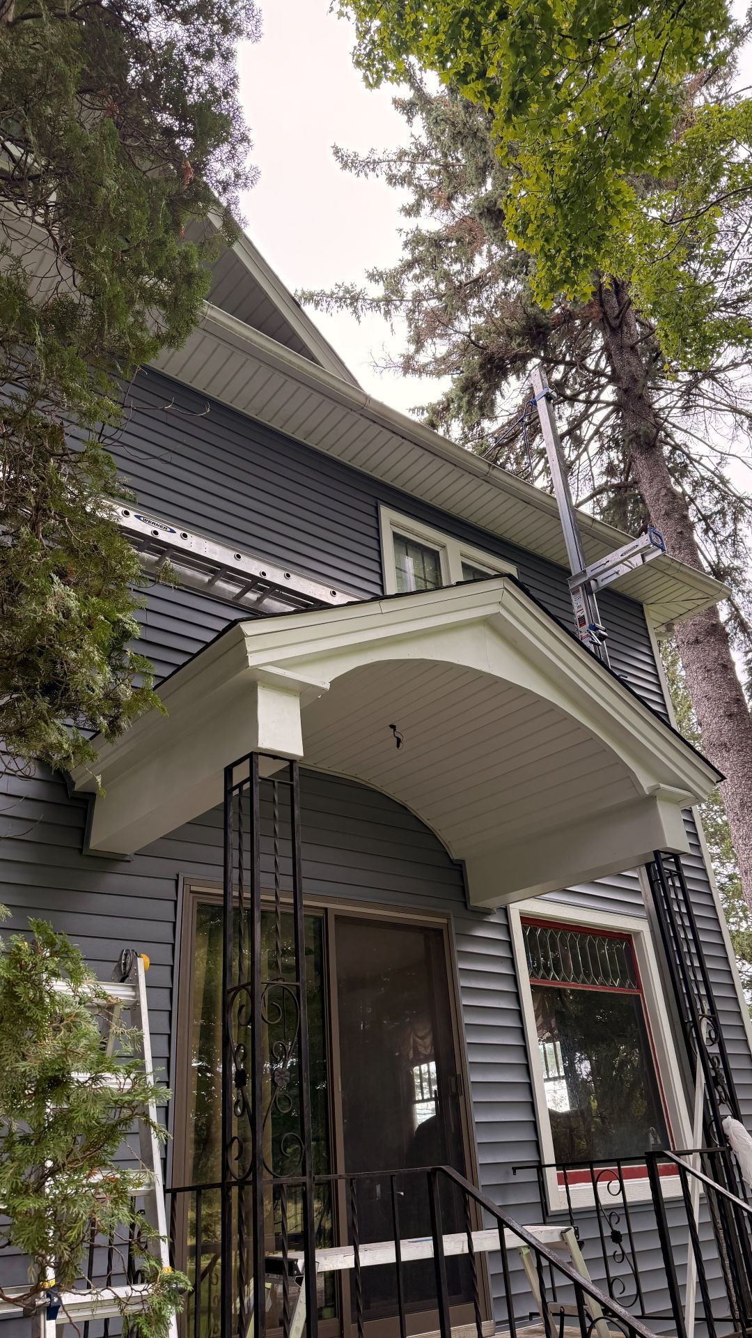 A gray, two-story house with a white arched entryway, a dark door, and black iron porch pillars.