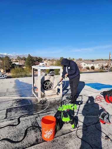 Person working with equipment on a rooftop beside an orange bucket and green machine under a clear blue sky