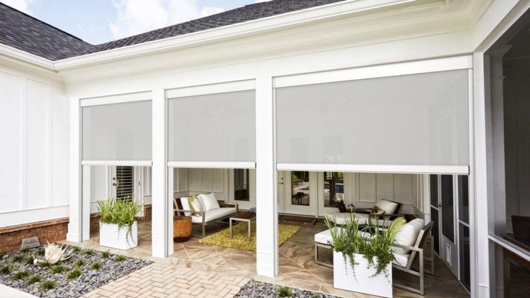 A screened in porch with a couch, chairs, and potted plants