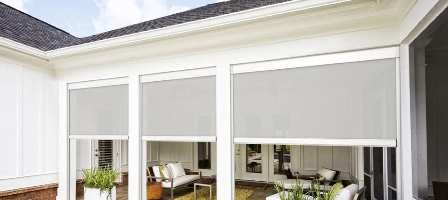 A screened in porch with white blinds on the windows and a living room