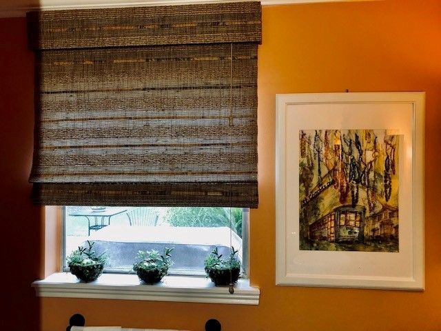 A window with a roman shade and a picture on the wall