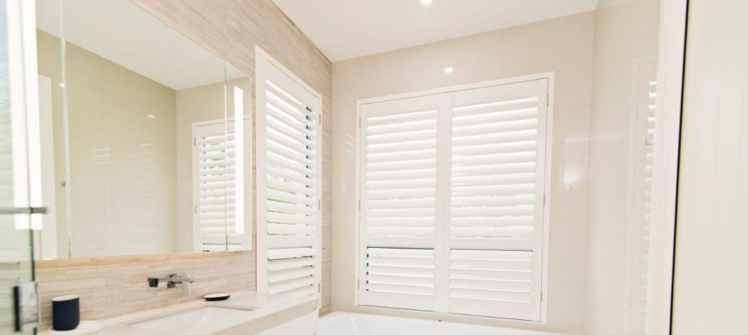A bathroom with a tub, sink, mirror and shutters