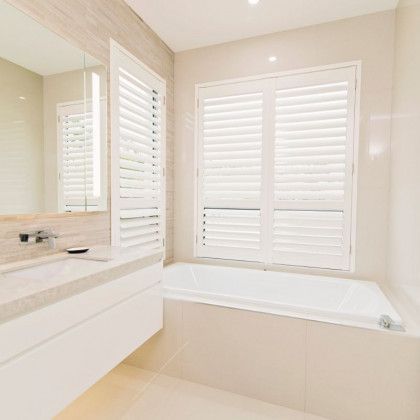 A bathroom with a sink, tub, mirror and shutters