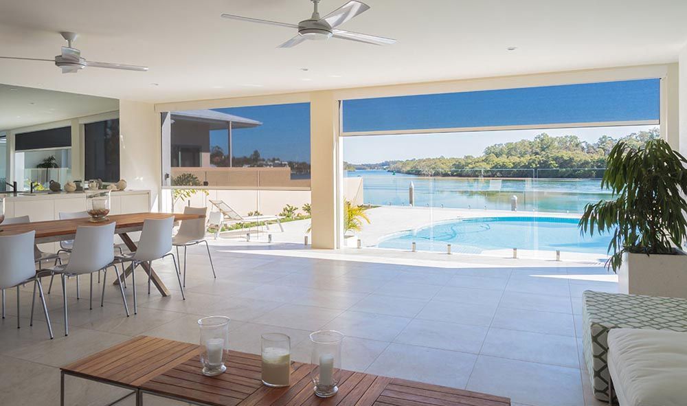 A living room with a table and chairs and a ceiling fan overlooking a swimming pool