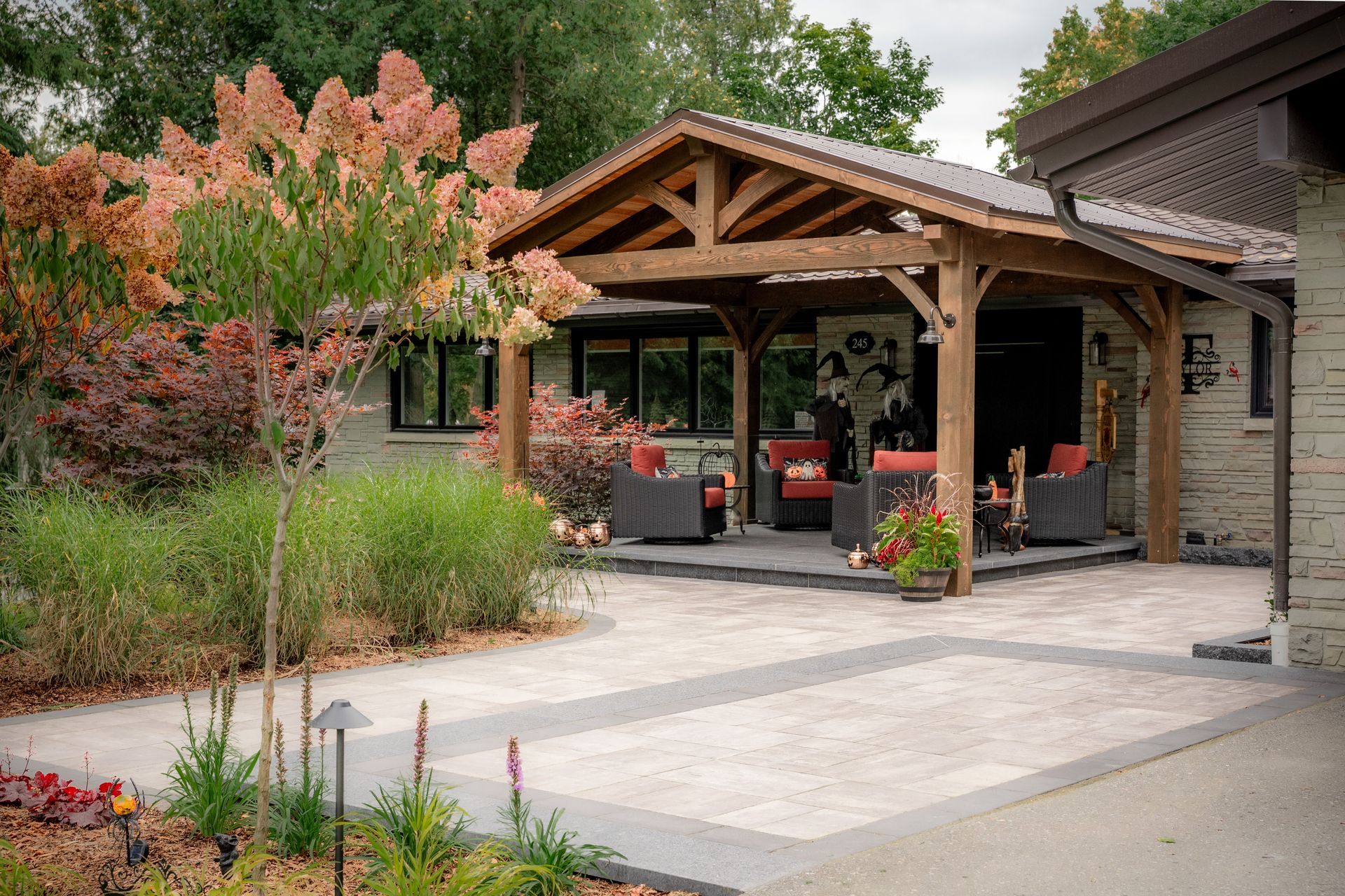 Front entrance landscape design with layered garden beds, timber pavilion, and expansive Unilock