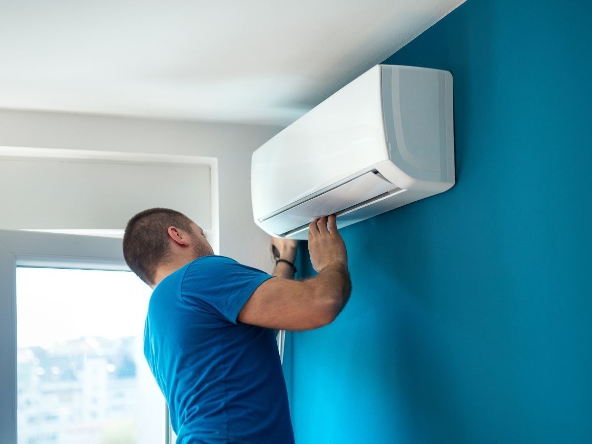 Technician installing a white wall-mounted air conditioner in a room with a teal accent wall.
