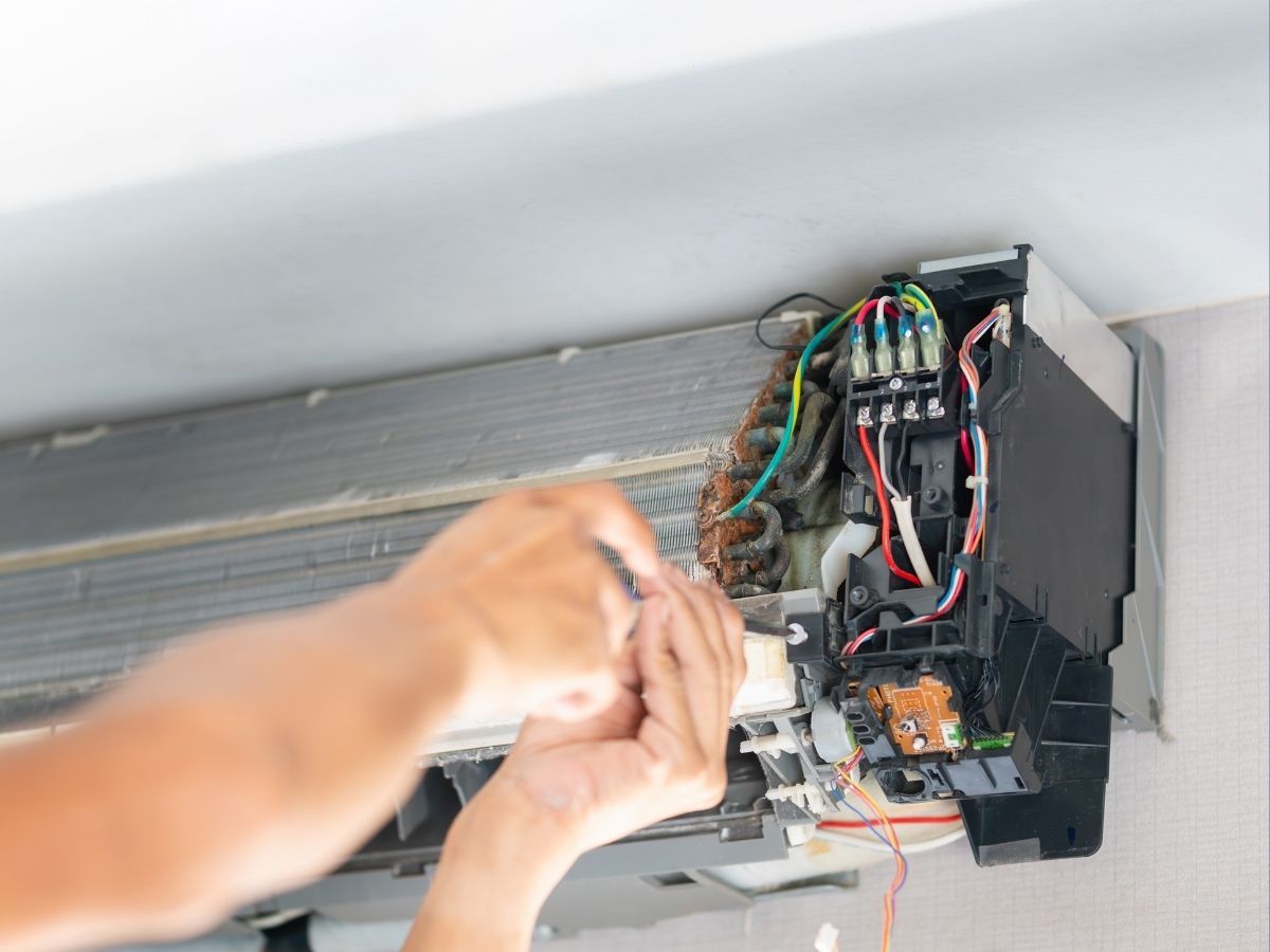 Person repairing exposed electrical wiring inside a wall-mounted panel.