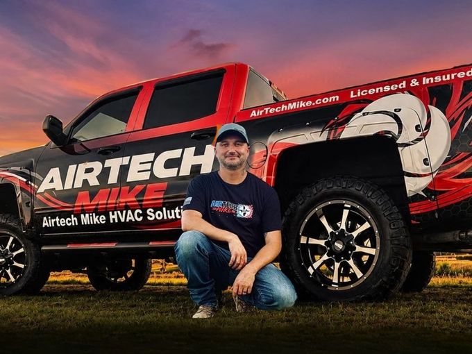 Man kneeling beside a black-and-red Arctic Air truck with large logo graphics at sunset