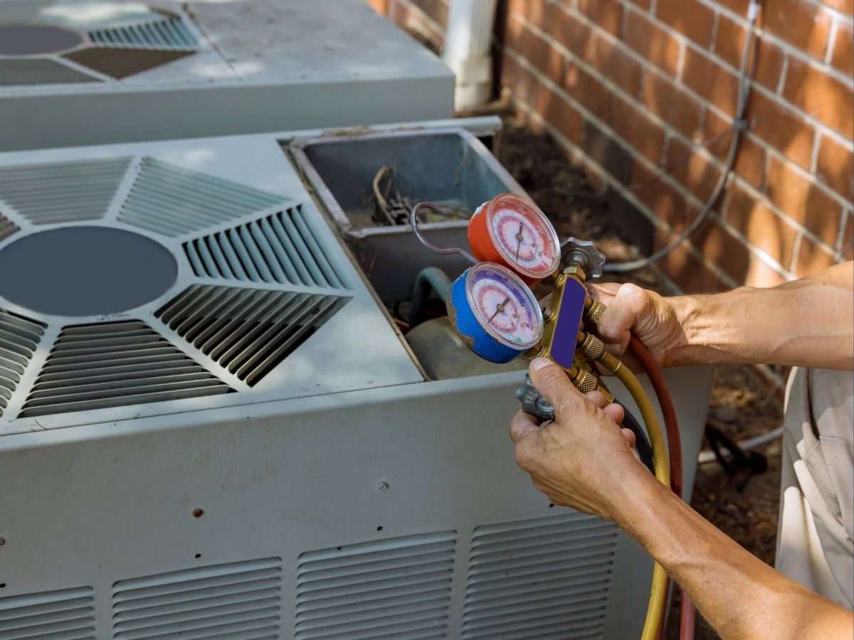 Technician connecting gauges to an outdoor air conditioner unit for servicing.