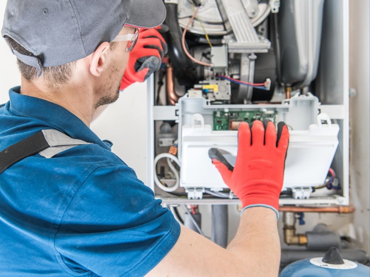 Technician in blue shirt and red gloves inspecting machinery inside an open equipment panel