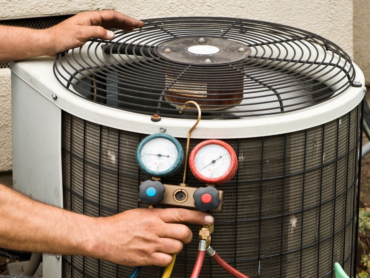HVAC technician checking outdoor AC unit with pressure gauges and hoses