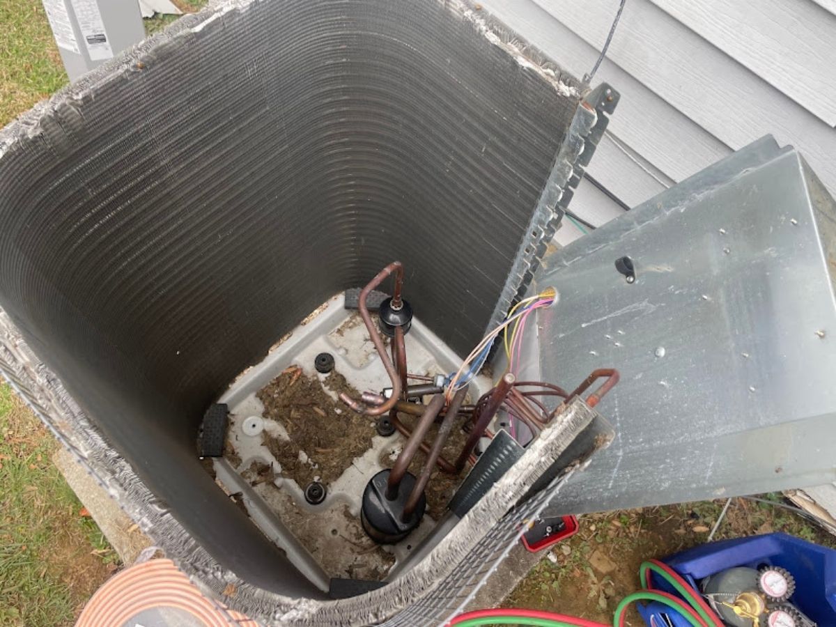 Open HVAC unit with exposed wiring and debris inside, next to a house wall.