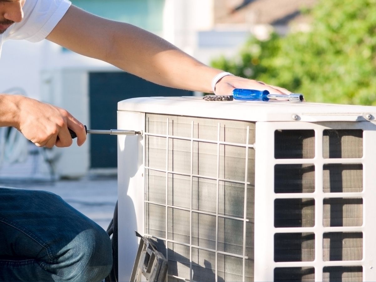 Technician cleaning outdoor air conditioner unit with a brush and tool