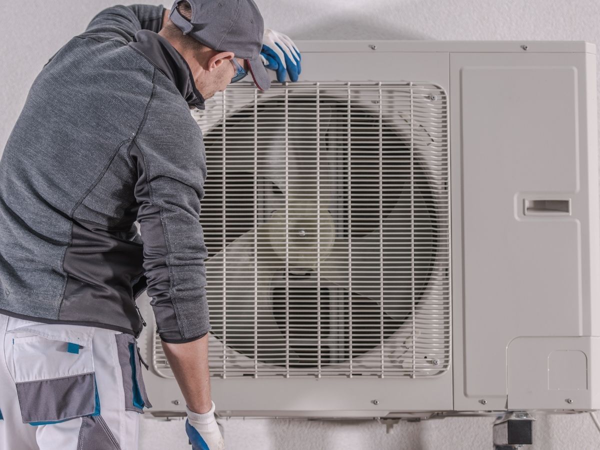 Technician inspecting an outdoor HVAC unit with a large fan