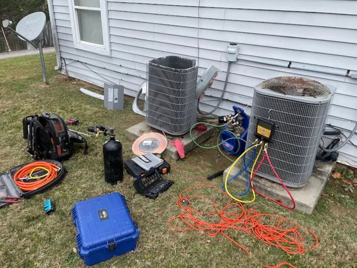 Outdoor HVAC equipment and tools scattered beside a house, with tangled red wires and two large units.