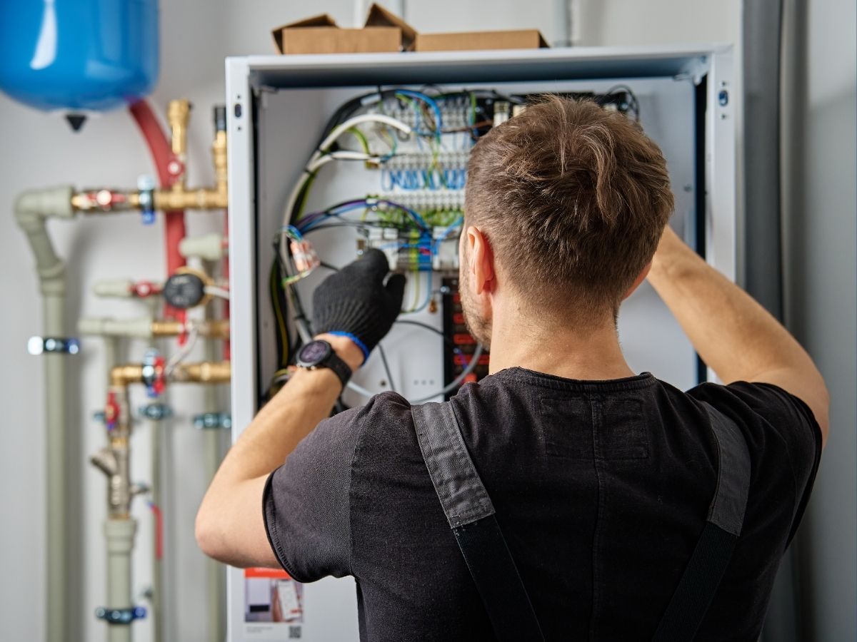 Technician in black gloves inspecting electrical wiring inside an open wall panel indoors