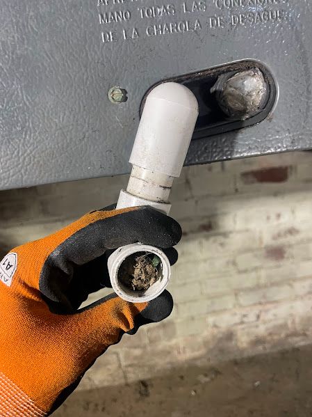 Gloved hand holding a broken white PVC pipe fitting near a wall opening with exposed wiring