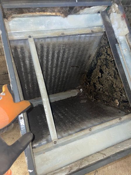 Dirty air filter inside a metal HVAC unit, with a gloved hand pointing at the clogged section.