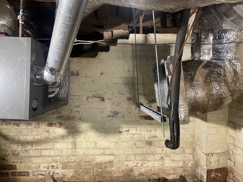 Basement with exposed pipes, ductwork, and a brick wall, with one wall covered in foil insulation.