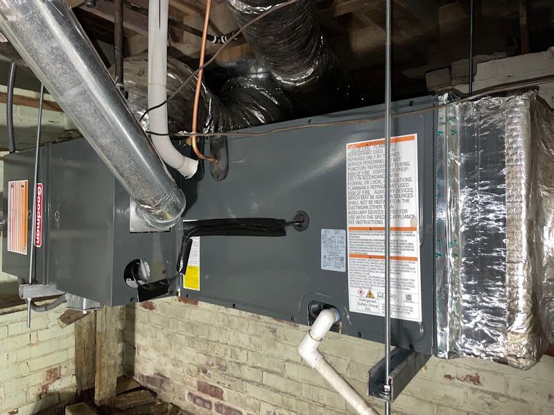 HVAC furnace and ductwork in a basement against a brick wall