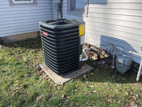 Outdoor air conditioner unit beside a house, with gray siding and utility meters nearby.