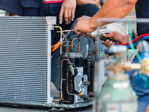 Technicians repairing an outdoor air conditioner condenser unit with tools and copper tubing