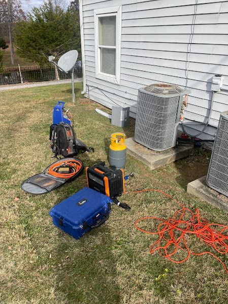 Tools and cords on a lawn beside a white house, with a blue case, orange cords, and a satellite dish.