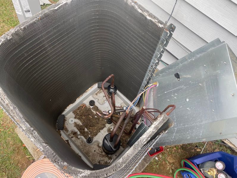 Open HVAC unit with exposed wiring and metal panel beside a house exterior.