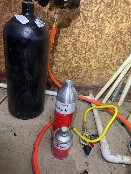 Black gas cylinder beside two small red-and-silver canisters and hoses against a wall