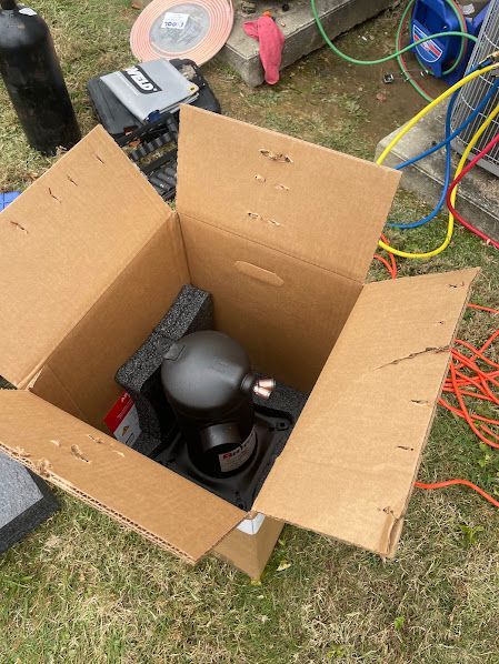 Open cardboard box holding a black helmet and gear on grass, with hoses and cords nearby.