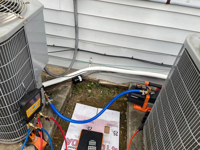 Outdoor HVAC units connected by blue and red service hoses on a concrete pad.