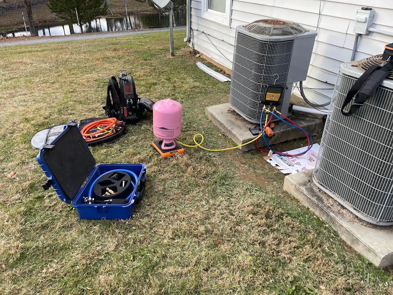 Open blue tool case, coiled cables, and HVAC units on a grassy yard beside a house.