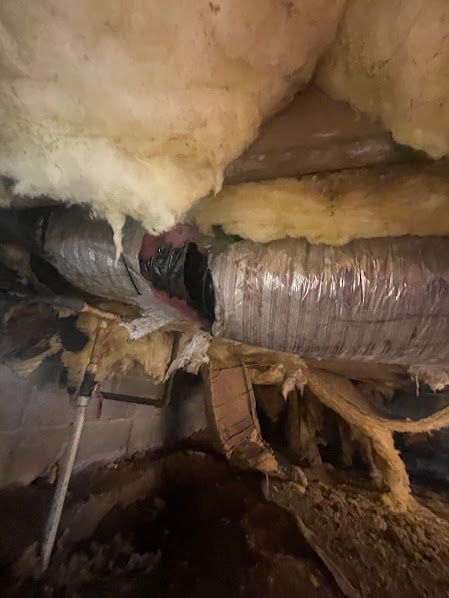 Damaged attic insulation and torn ductwork with exposed framing and debris