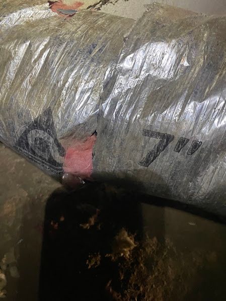 Metal duct wrapped in silver insulation with pink tape marks above a dark opening.
