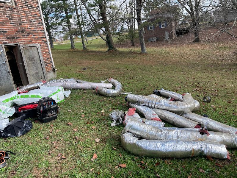Pile of silver flexible ducting and debris beside a brick building on a grassy yard.