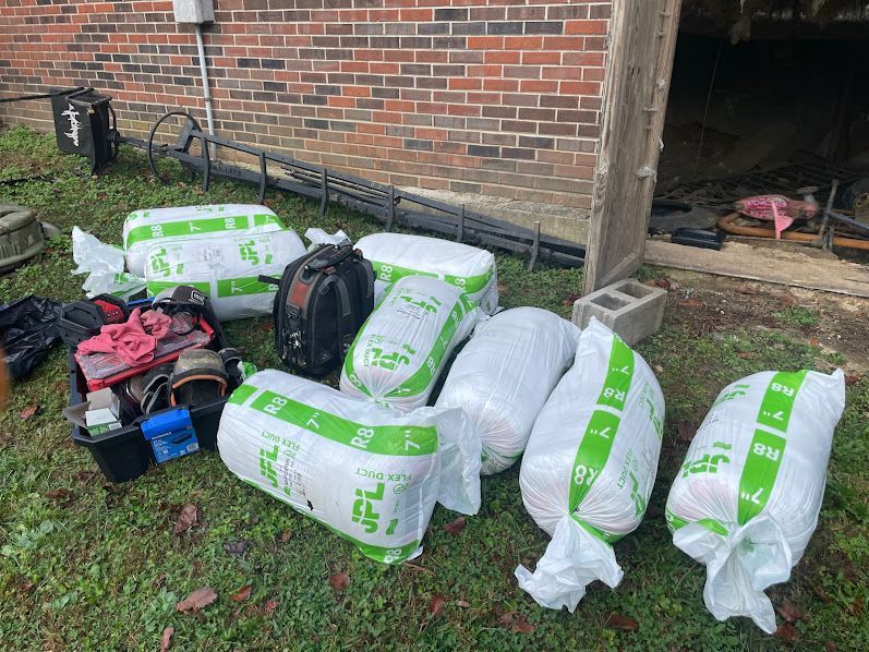 Wrapped parcels and tools stacked on grass beside a brick wall and open shed.