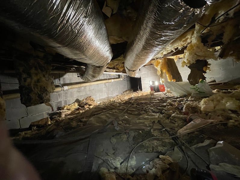 Collapsed building interior with debris, hanging ductwork, and a small red light in the distance
