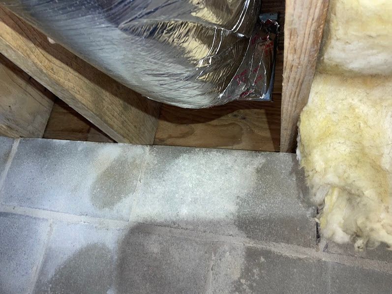 Attic insulation and ductwork beside wooden rafters, with fiberglass insulation and vapor barrier visible