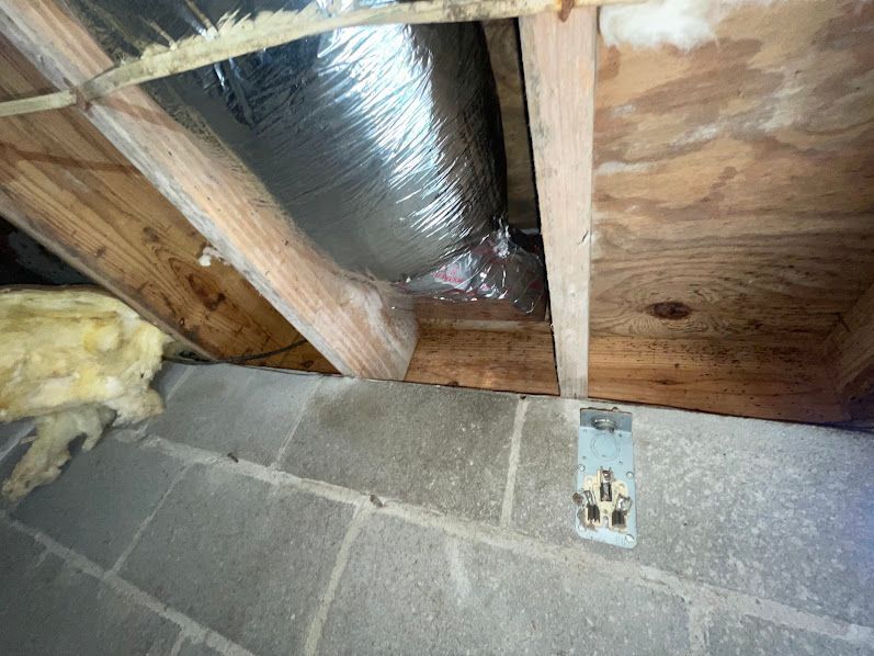 Exposed attic framing with duct insulation above cinder block wall and electrical outlet.