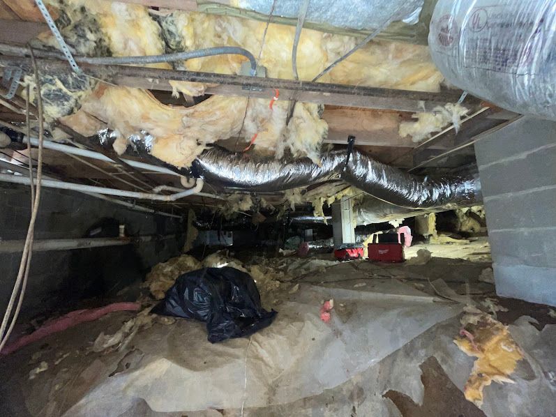 Crawlspace with exposed insulation, ducts, pipes, and a black trash bag on the floor
