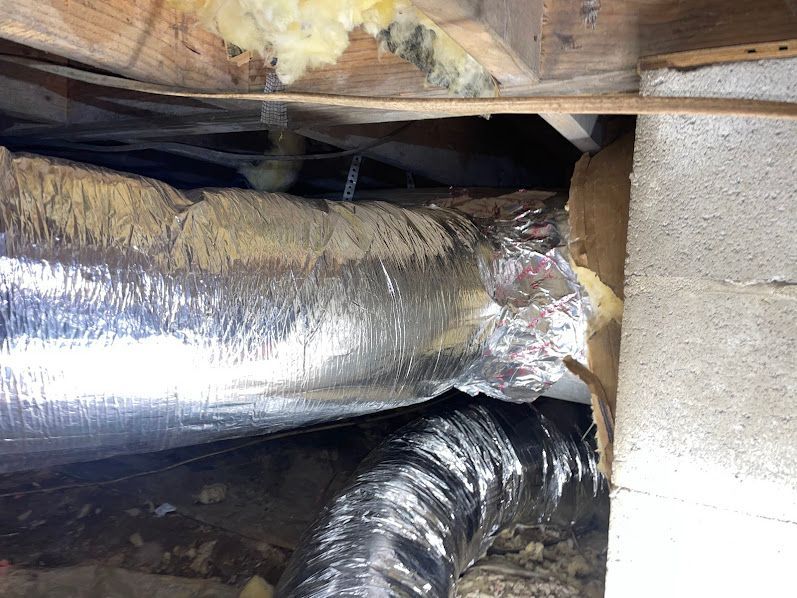 Foil-wrapped HVAC ducts in a cramped attic crawlspace with insulation and wooden beams