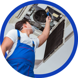 Technician in blue overalls servicing an air conditioner unit overhead