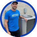 HVAC technician in blue shirt standing beside an outdoor air conditioner unit