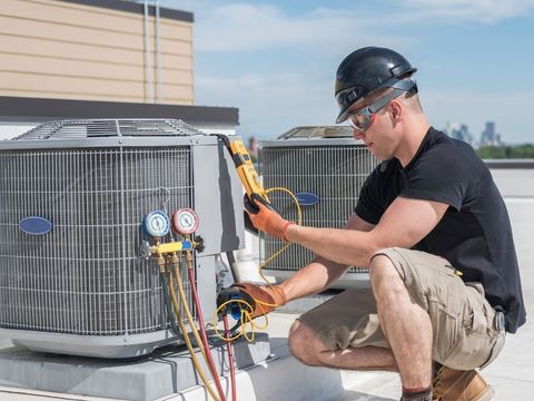 Technician servicing outdoor HVAC unit with gauges and tools on a rooftop.