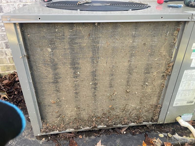 Dirty outdoor HVAC condenser unit with a clogged, dust-covered coil beside a brick wall.
